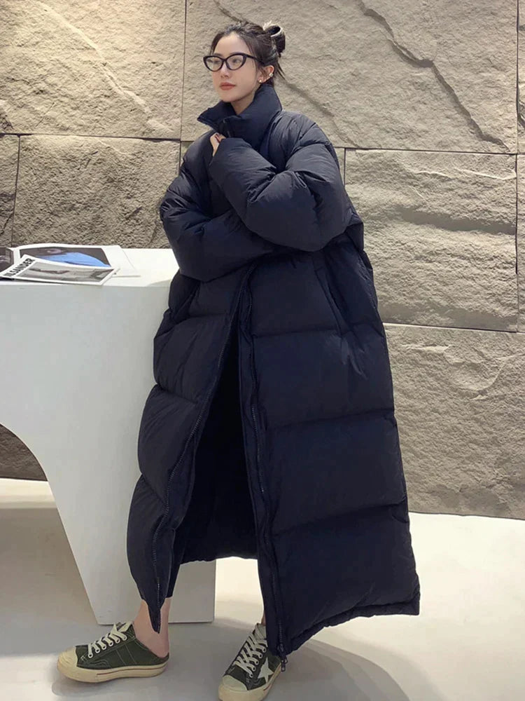 Frau in übergroßem, schwarzem Daunenmantel, modisch und warm, steht vor modernem Hintergrund. Wintermode, Damenbekleidung, stilvoll.