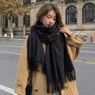 Frau in beigem Mantel mit schwarzem Schal auf städtischer Straße. Herbstmode, eleganter Look, Damenbekleidung, stilvoller Mantel, Accessoires.