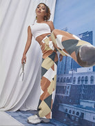 Frau in modischer, geometrisch gemusterter Hose und weißem Crop-Top posiert vor urbanem Hintergrund. Trendige Streetwear, stilvolle Mode.