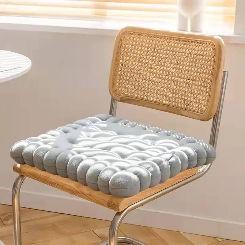 Moderner Stuhl mit grauem, gepolstertem Sitzkissen und geflochtener Rückenlehne im Sonnenlicht.