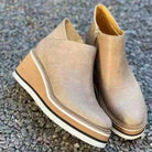 Beige Keilabsatz-Stiefeletten aus Leder auf Kieselsteinen, modisch und bequem, ideal für Herbstmode. Damenstiefel, trendige Schuhe.