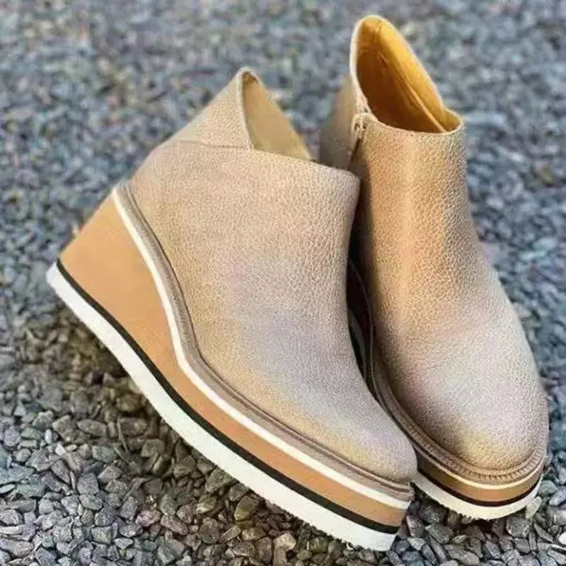 Beige Keilabsatz-Stiefeletten aus Leder auf Kieselsteinen, modisch und bequem, ideal für Herbstmode. Damenstiefel, trendige Schuhe.