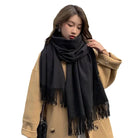 Damenmode: Eleganter schwarzer Schal mit Fransen, kombiniert mit beigem Mantel. Perfekt für Herbst und Winter. Trendig, warm und stilvoll.