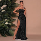 Elegantes schwarzes Abendkleid mit hohem Beinschlitz, getragen von einer Frau vor tropischen Pflanzen. Perfekt für formelle Anlässe und Events.