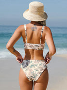 Frau im geblümten Bikini am Strand, Strohhut, Rückansicht. Sommermode, Strandbekleidung, Urlaub, Bademode, stilvoll, Meereshintergrund.