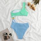 Grüner und blauer Bikini aus Strickstoff auf weißem Hintergrund mit Blumen und Sonnenbrille.