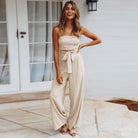 Frau in elegantem, beigefarbenem Jumpsuit vor weißer Tür. Modetrend, Damenmode, Sommeroutfit, stilvoll, lässig, schick.