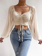 Damen-Crop-Top mit langen Ärmeln und Raffung, kombiniert mit modischen Jeans. Perfekt für trendige Outfits und stilvolle Freizeitlooks.