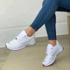Damen-Sneaker in Weiß mit goldenen Akzenten, kombiniert mit blauen Jeans. Bequeme Freizeitschuhe, ideal für Alltag und Sport.