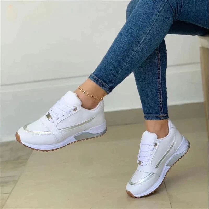 Damen-Sneaker in Weiß mit goldenen Akzenten, kombiniert mit blauen Jeans. Bequeme Freizeitschuhe, ideal für Alltag und Sport.