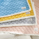 Vier bunte, gesteppte Babydecken mit weichem Rand, in Blau, Gelb, Grau und Rosa.