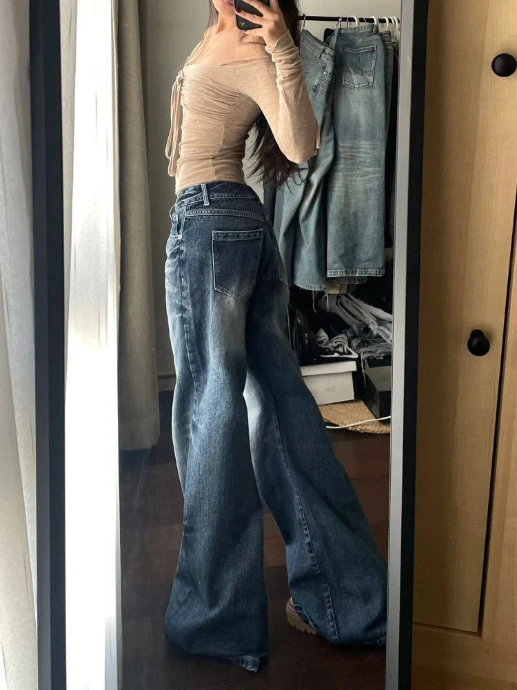 Frau in weitem, hochtailliertem Jeanshose und beigem Oberteil posiert vor einem Spiegel. Modetrend, lässiger Stil, Denim, Streetwear.