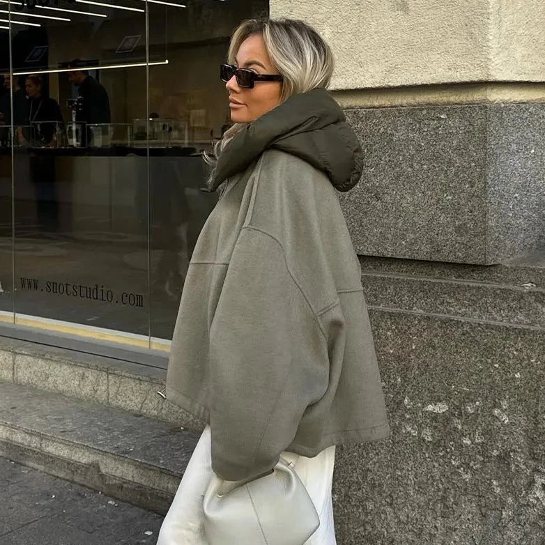 Frau in übergroßer, grauer Jacke mit Kapuze und Sonnenbrille, hält weiße Tasche. Streetstyle, Mode, urbaner Look, Herbstmode, Damenbekleidung.