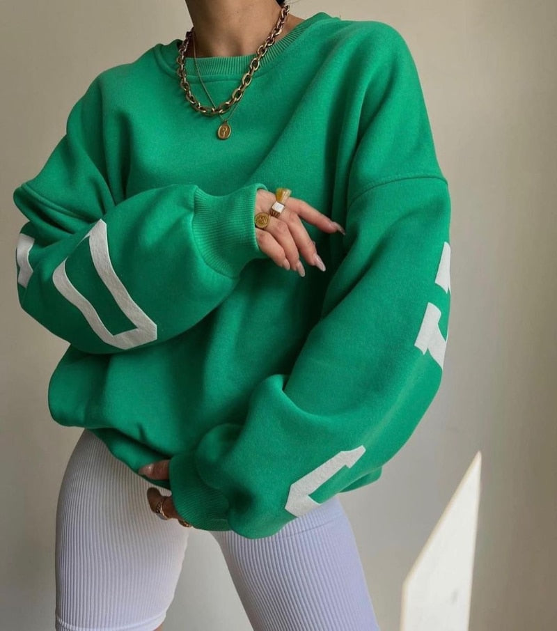Grüner Oversize-Pullover mit weißen Streifen, kombiniert mit goldener Halskette und Ringen. Modetrend, Streetwear, lässiger Stil.