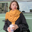 Frau mit gelbem Schal und schwarzem Mantel hält einen Kaffeebecher vor einem grünen Auto. Herbstmode, Streetstyle, Accessoires, urbaner Look.