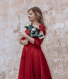 Frau in rotem Kleid hält Blumenstrauß vor rustikaler Wand. Elegantes Outfit, romantische Atmosphäre, Modefotografie, Blumen, rotes Kleid.