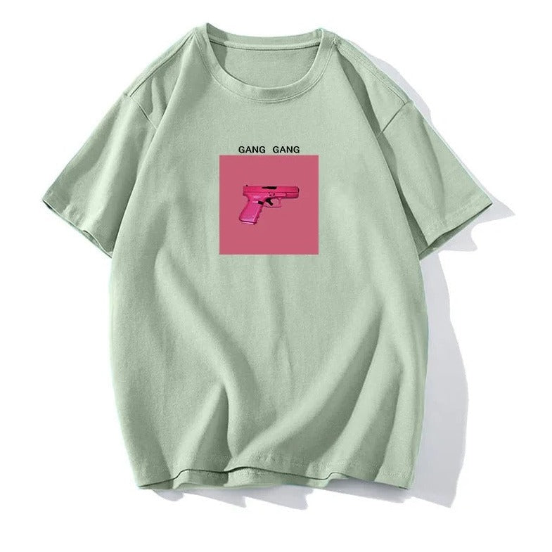 Grünes T-Shirt mit pinkem Pistolen-Print und "Gang Gang"-Schriftzug. Trendige Streetwear, lässiger Stil, modisches Design.
