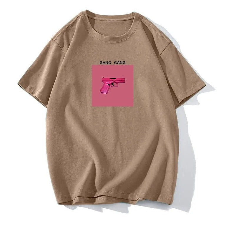 Beiges T-Shirt mit pinkem Pistolen-Print und "Gang Gang"-Schriftzug. Trendige Streetwear, lässiger Stil, ideal für urbane Modefans.