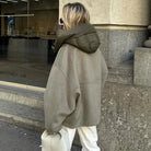 Frau in übergroßer, olivgrüner Jacke mit Kapuze, steht vor einem Schaufenster. Modetrend, Wintermode, Streetstyle, lässiger Look.