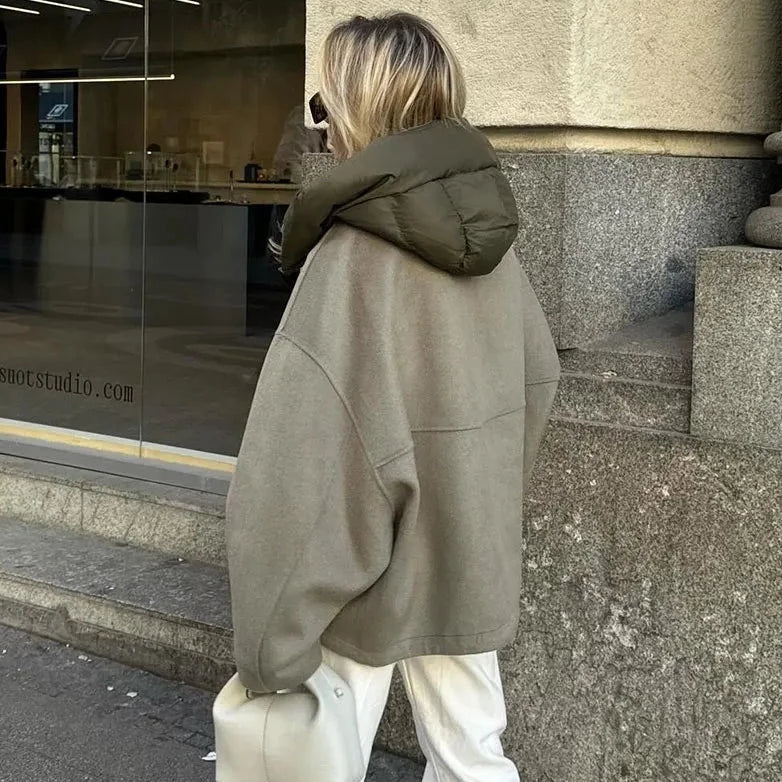 Frau in übergroßer, olivgrüner Jacke mit Kapuze, steht vor einem Schaufenster. Modetrend, Wintermode, Streetstyle, lässiger Look.