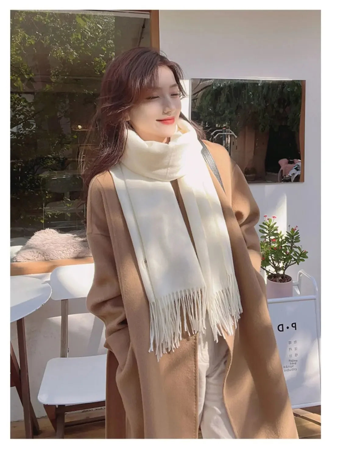 Frau in elegantem, beigem Mantel und weißem Schal, lächelnd im Freien. Modetrend Herbst/Winter, stilvolle Damenbekleidung, Outdoor-Mode.