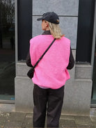 Frau in pinker Weste und schwarzer Kappe, steht vor grauer Wand. Modetrend, Streetstyle, lässiger Look, Herbstmode, urbaner Stil.