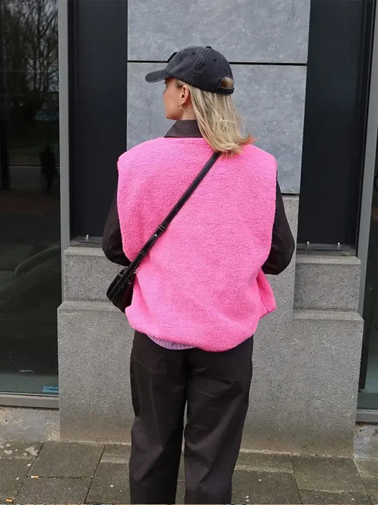 Frau in pinker Weste und schwarzer Kappe, steht vor grauer Wand. Modetrend, Streetstyle, lässiger Look, Herbstmode, urbaner Stil.