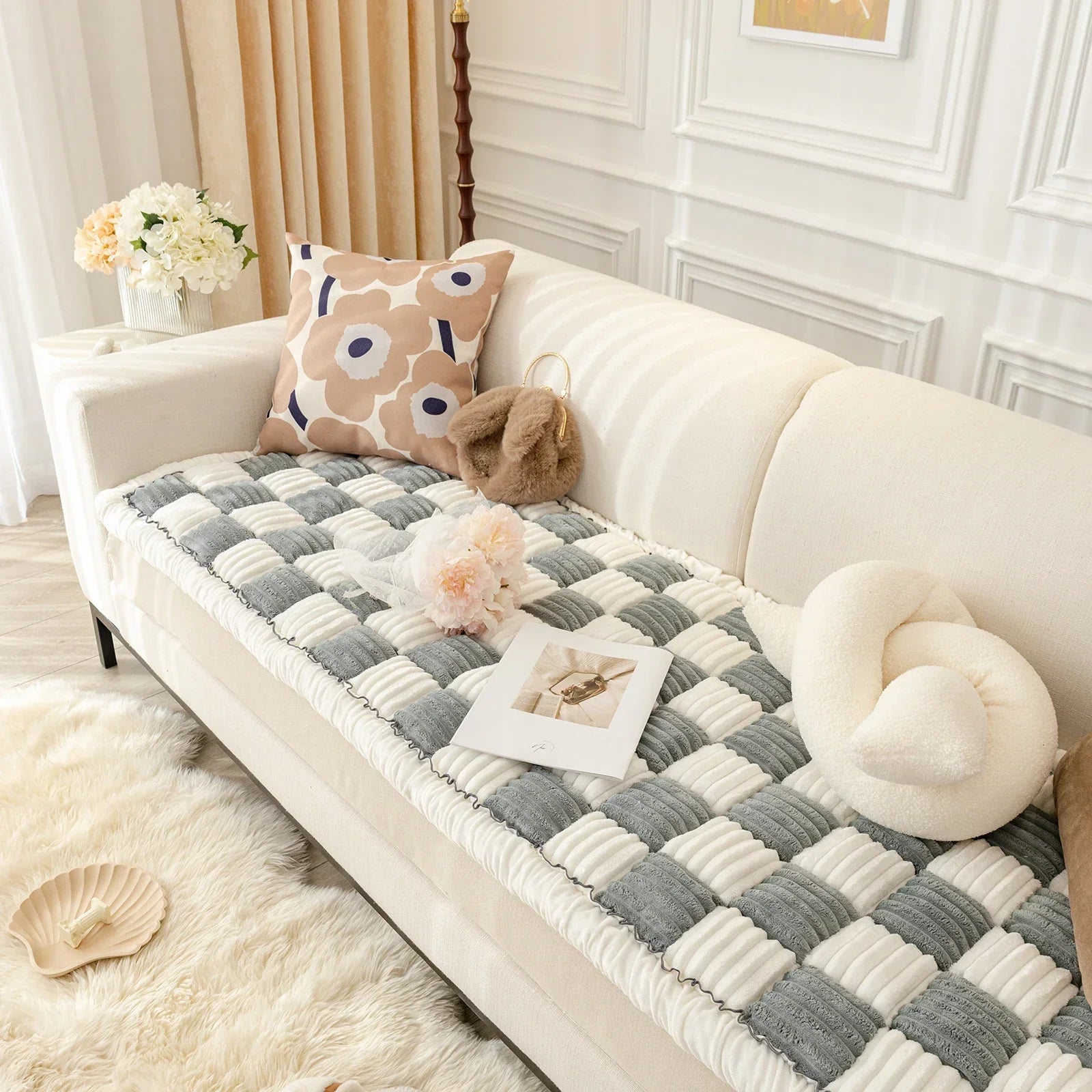 Beige Sofa mit kariertem Überwurf, dekorativen Kissen und Blumen, skandinavisches Wohnzimmer.