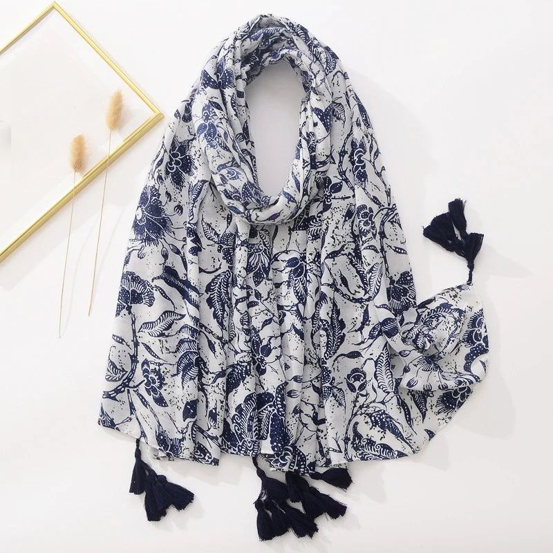 Eleganter weißer Schal mit blauem Blumenmuster und Quasten, ideal für Damenmode. Perfektes Accessoire für Frühling und Sommer.
