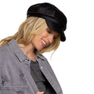 Frau mit schwarzer Leder-Baker-Boy-Mütze und grauer Jacke. Modetrend, stilvolles Accessoire, urbaner Look, Damenmode, Herbstoutfit.