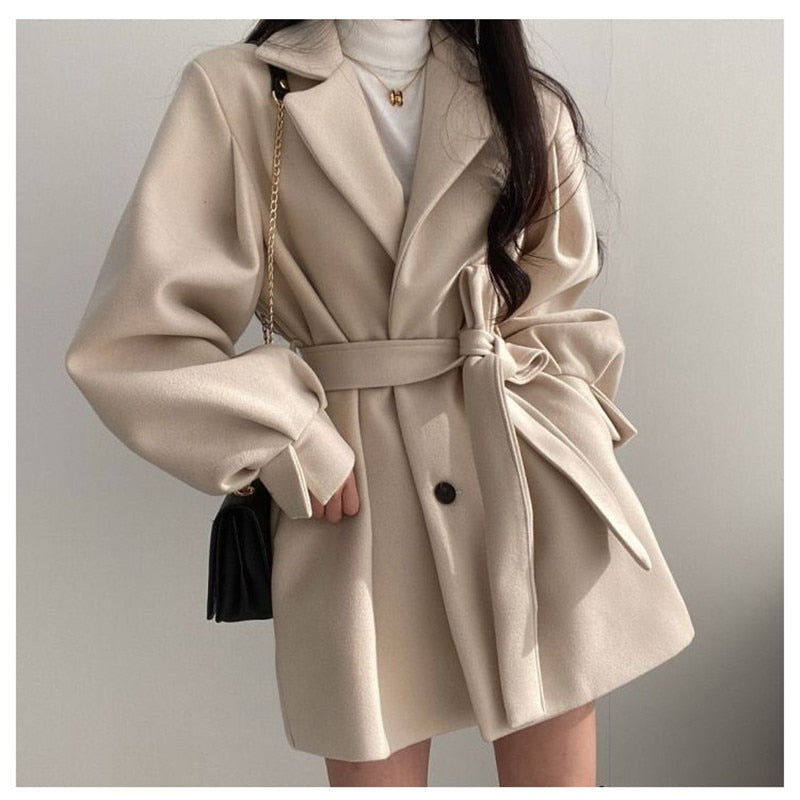 Eleganter beiger Wollmantel für Damen, tailliert mit Gürtel, ideal für Herbstmode. Stilvoller Look mit schwarzer Handtasche und weißem Rollkragenpullover.