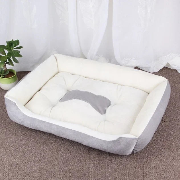 Graues und weißes Hundebett aus Plüsch, rechteckig, auf Teppichboden vor Vorhang.