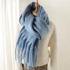 Weicher, blauer Schal aus Kaschmir mit Fransen, drapiert über einem cremefarbenen Pullover. Perfekt für Wintermode und stilvolle Accessoires.