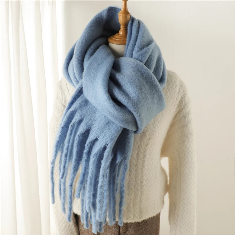 Weicher, blauer Schal aus Kaschmir mit Fransen, drapiert über einem cremefarbenen Pullover. Perfekt für Wintermode und stilvolle Accessoires.