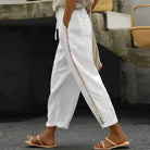 Weiße Leinenhose mit seitlichem Häkelmuster, lässig geschnitten, ideal für Sommermode. Perfekt kombiniert mit Sandalen für einen entspannten Look.