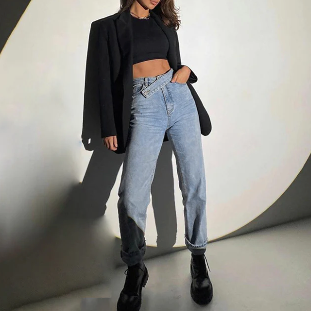 Frau in schwarzem Blazer und Crop-Top, kombiniert mit blauen High-Waist-Jeans und schwarzen Stiefeln. Modetrend, Streetstyle, lässig.