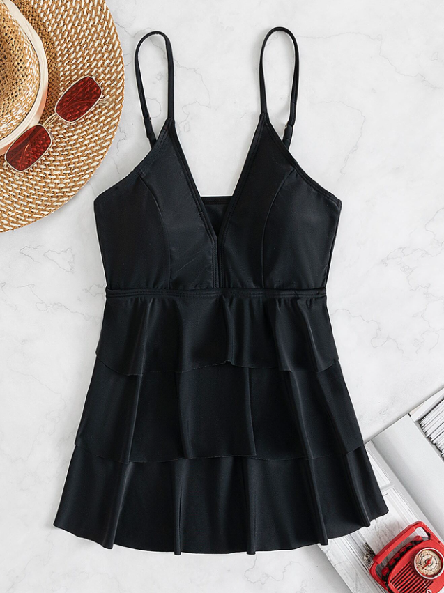 Schwarzes, ärmelloses Sommerkleid mit V-Ausschnitt und Rüschen, ideal für Strandmode. Perfekt kombiniert mit Strohhut und Sonnenbrille.