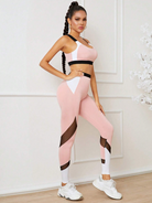 Frau in rosa-weißem Sportoutfit mit schwarzen Akzenten, posiert vor weißer Wand. Fitnessmode, Sportbekleidung, athletischer Look.