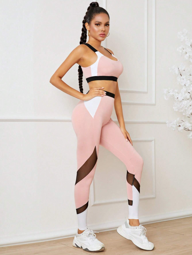 Frau in rosa-weißem Sportoutfit mit schwarzen Akzenten, posiert vor weißer Wand. Fitnessmode, Sportbekleidung, athletischer Look.