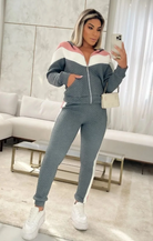 Frau in grauem Jogginganzug mit weiß-rosa Streifen, posiert im Wohnzimmer. Bequemes Freizeitoutfit, ideal für Zuhause oder Sport.
