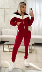 Frau in rotem Trainingsanzug mit weißen Streifen, posiert vor einem Sofa. Modetrend, Freizeitkleidung, sportlich-elegant, Selfie.