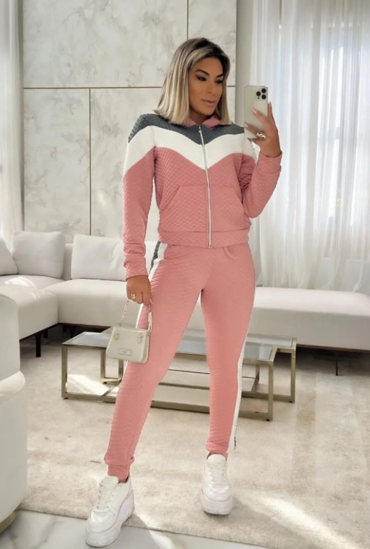 Frau in rosa Trainingsanzug mit weiß-grauen Details, posiert im Wohnzimmer. Beliebte Mode, Freizeitkleidung, Selfie, stilvoll, modern.