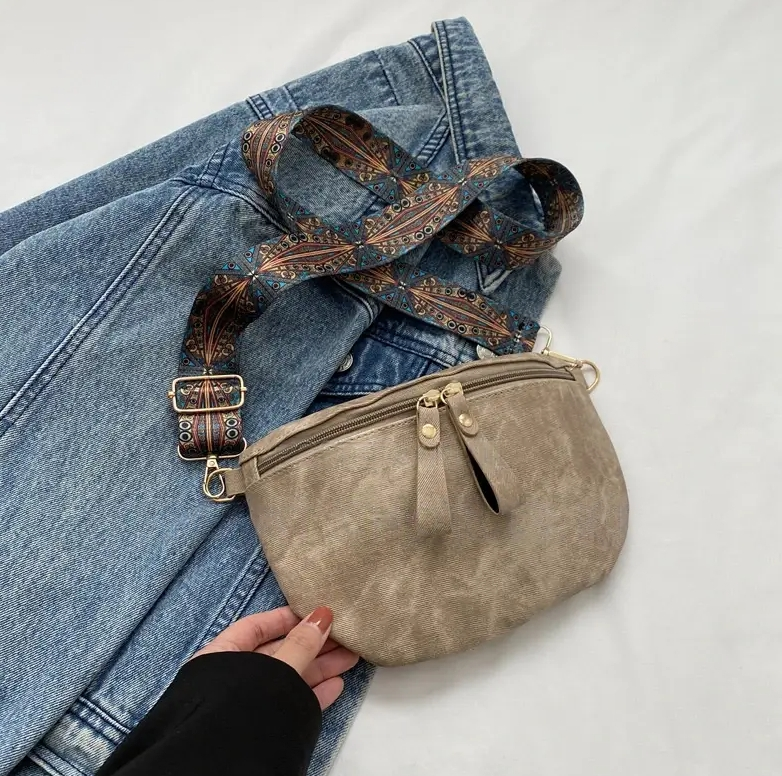 Beige Umhängetasche mit verstellbarem, gemustertem Riemen auf Jeansstoff. Modisch, vielseitig, ideal für Alltag und Reisen.