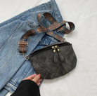 Schwarze Leder-Gürteltasche mit verstellbarem, gemustertem Riemen auf blauer Jeans. Modisches Accessoire, ideal für Reisen und Alltag.