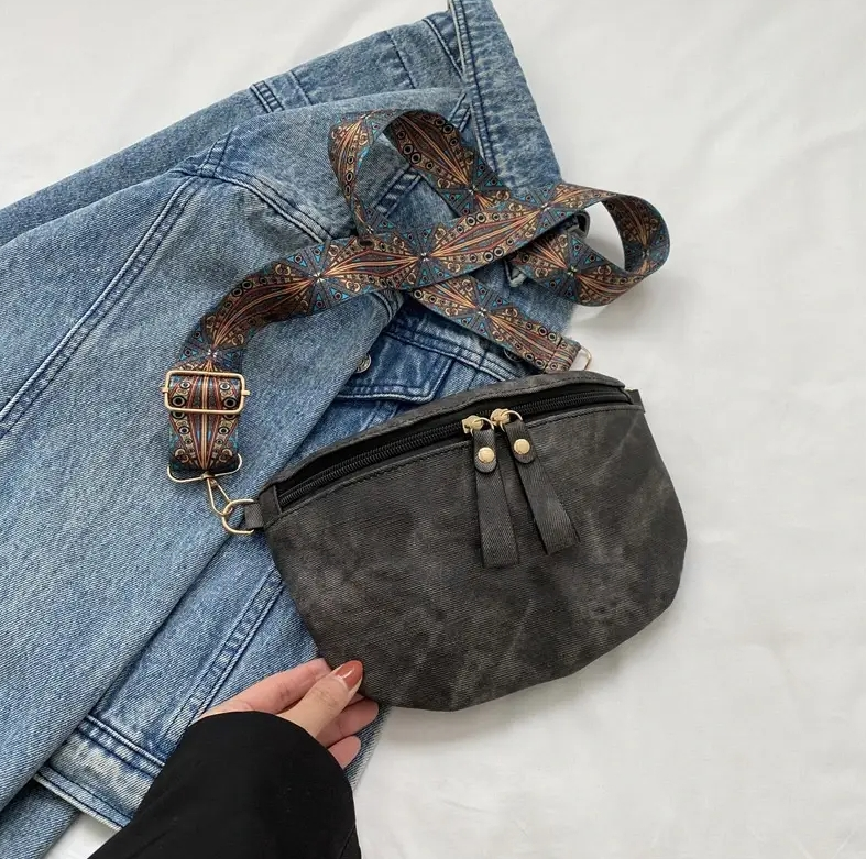 Schwarze Leder-Gürteltasche mit verstellbarem, gemustertem Riemen auf blauer Jeans. Modisches Accessoire, ideal für Reisen und Alltag.