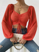 Rotes, langärmliges Crop-Top mit Raffung, kombiniert mit blauer Jeans und weißer Clutch. Modetrend, Damenmode, stilvolles Outfit.