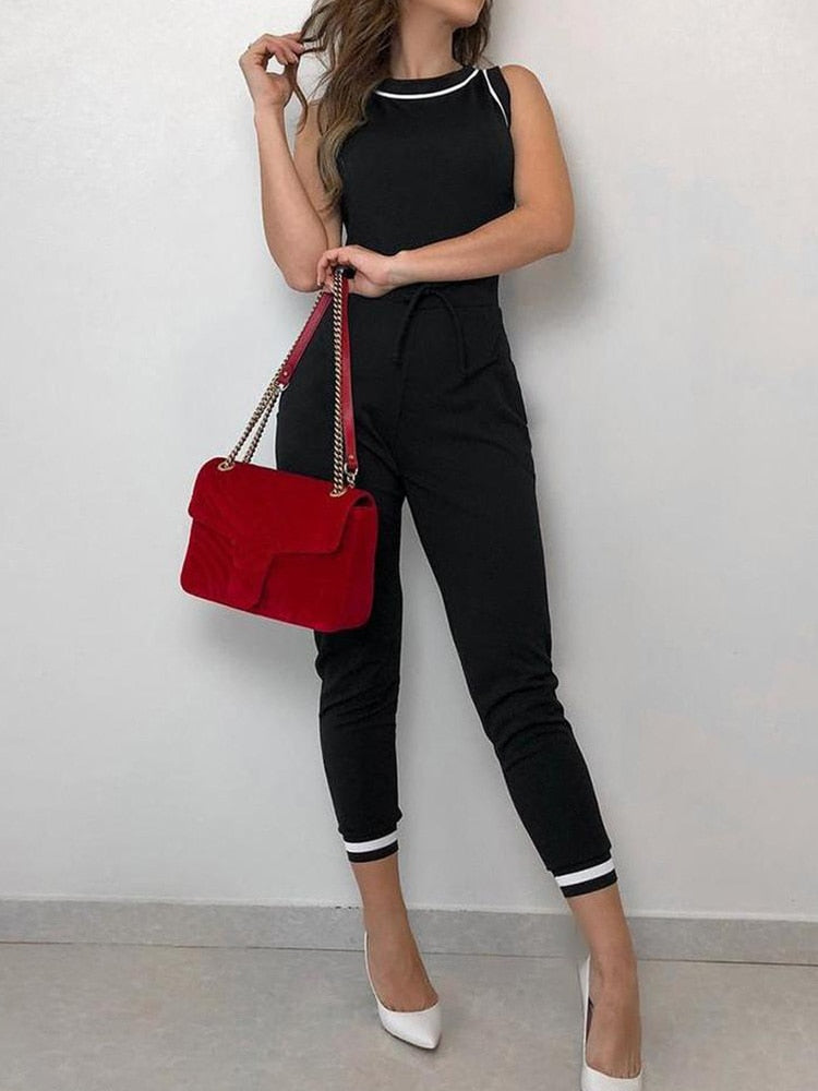 Frau in schwarzem Jumpsuit mit weißem Saum, hält rote Handtasche, trägt weiße High Heels. Elegante Damenmode, stilvolles Outfit.