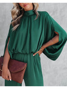 Elegantes Damenkleid in Smaragdgrün mit Fledermausärmeln, kombiniert mit einer braunen Clutch. Perfekt für stilvolle Anlässe und Modebewusste.