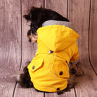 Hund in gelber Regenjacke mit Kapuze, sitzt vor Holzhintergrund. Modische Hundebekleidung, wetterfest, stilvoll, Haustiermode, Hundemantel.