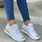 Weiße Damen-Sneaker mit goldenen Akzenten, kombiniert mit blauen Jeans. Modische Sportschuhe, ideal für Freizeit und Streetwear.